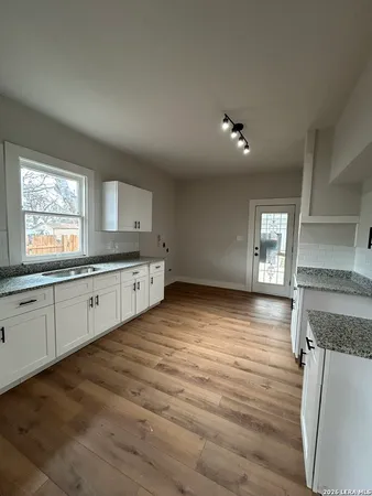 a kitchen with granite countertop a stove a sink and white cabinets with wooden floor