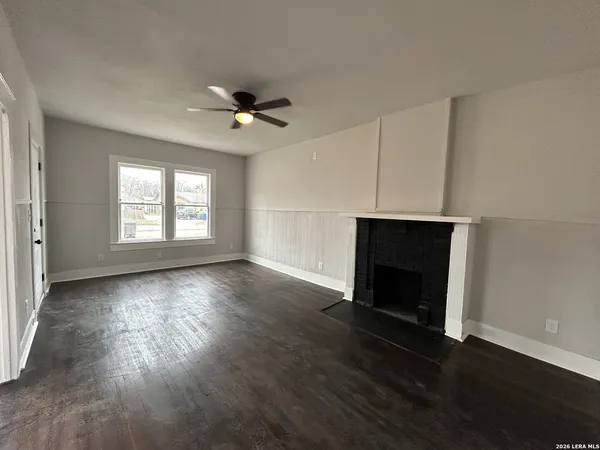 an empty room with wooden floor fireplace and windows