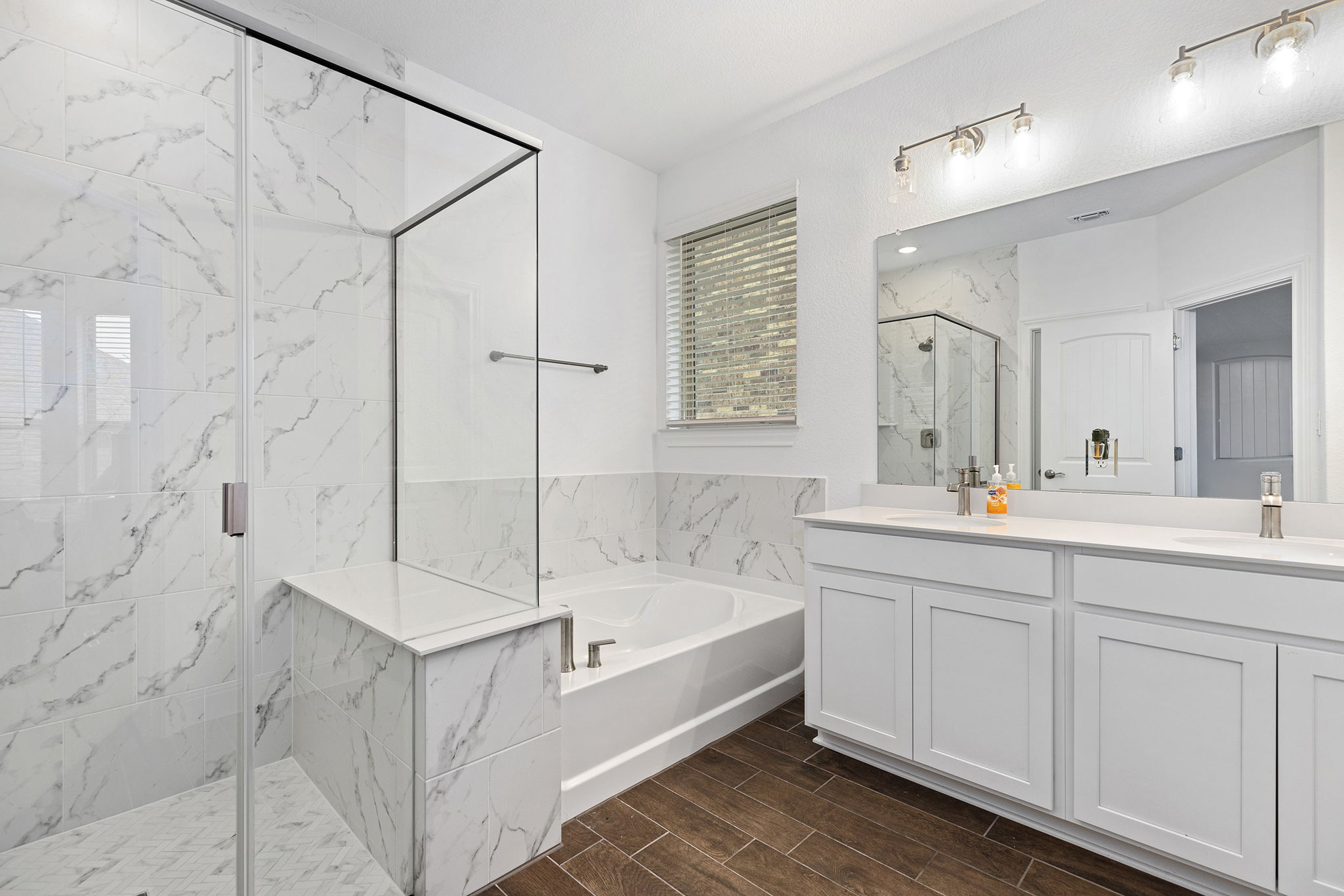 116 Raleigh Drive Georgetown, TX 78633 - Photo 13 of 28 Marble-look tile and wood-look flooring enhance this primary bathroom, featuring a dual vanity and glass-enclosed shower.