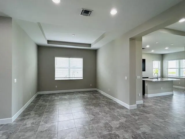an empty room with windows and view of kitchen