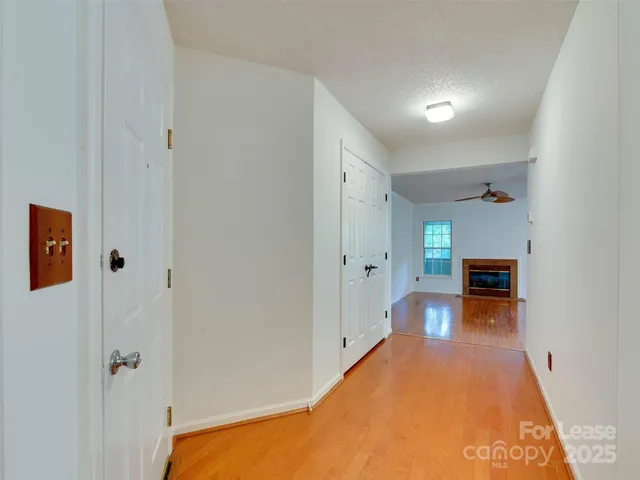 a view of a hallway to an empty room with wooden floor and fireplace