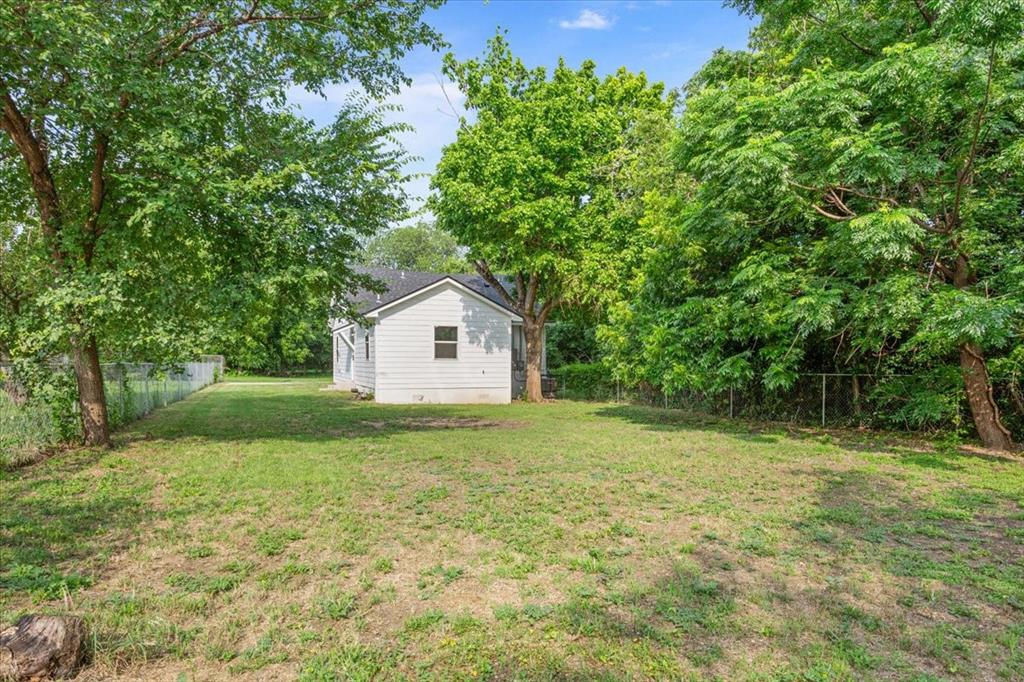 3109 North 20th Street Waco, TX 76708 - Photo 21 of 24 Expansive rear yard featuring a wire fence, mature trees, and a white siding exterior with a dark shingle roof