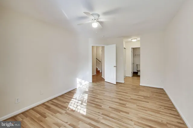 a view of an empty room with wooden floor and a ceiling fan