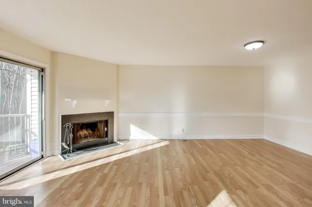 a view of an empty room with wooden floor fireplace and a window