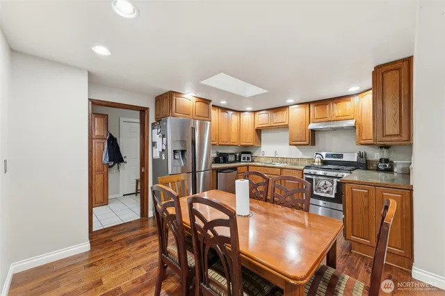 a kitchen with stainless steel appliances granite countertop a stove top oven a sink dishwasher and white cabinets with wooden floor