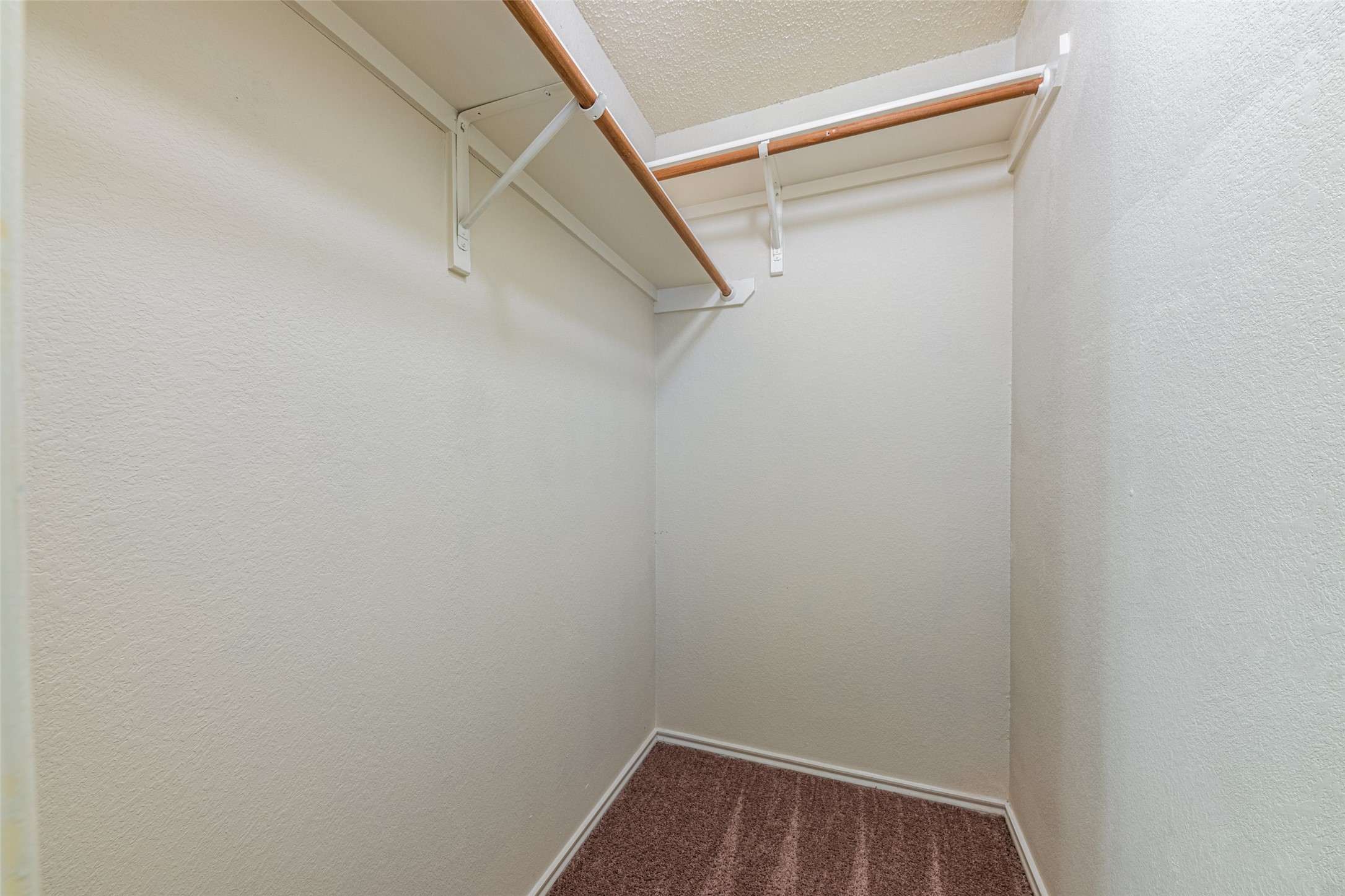 7216 Aldea Drive, Unit A Austin, TX 78745 - Photo 23 of 25 Walk-in closet featuring light beige walls, two wooden clothing rods, white shelving, and brown patterned carpet flooring