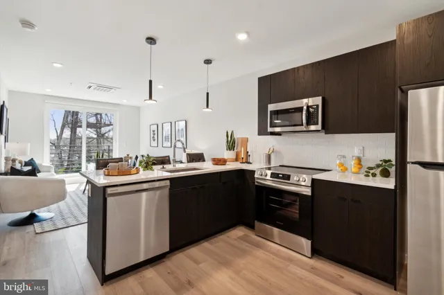 a kitchen with stainless steel appliances granite countertop a stove top oven a sink dishwasher a refrigerator and a dining table with wooden floor