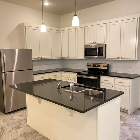 a kitchen with stainless steel appliances granite countertop a sink a stove a refrigerator a microwave oven with white cabinets