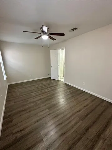 a view of an empty room with wooden floor and a ceiling fan