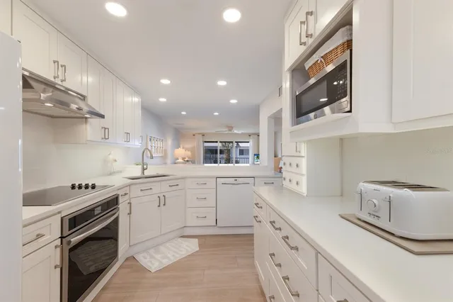 a kitchen with a sink dishwasher stove and white cabinets with wooden floor