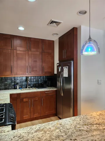 a kitchen with stainless steel appliances granite countertop a refrigerator a stove and a sink with wooden cabinets