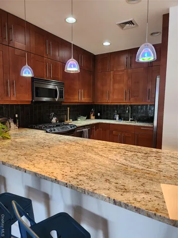 a kitchen with stainless steel appliances granite countertop a sink wooden cabinets and a wooden floor