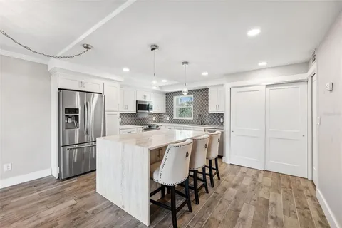 a kitchen with stainless steel appliances granite countertop a sink a stove a refrigerator a dining table and chairs with wooden floor