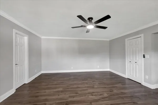 a view of an empty room with wooden floor and a ceiling fan
