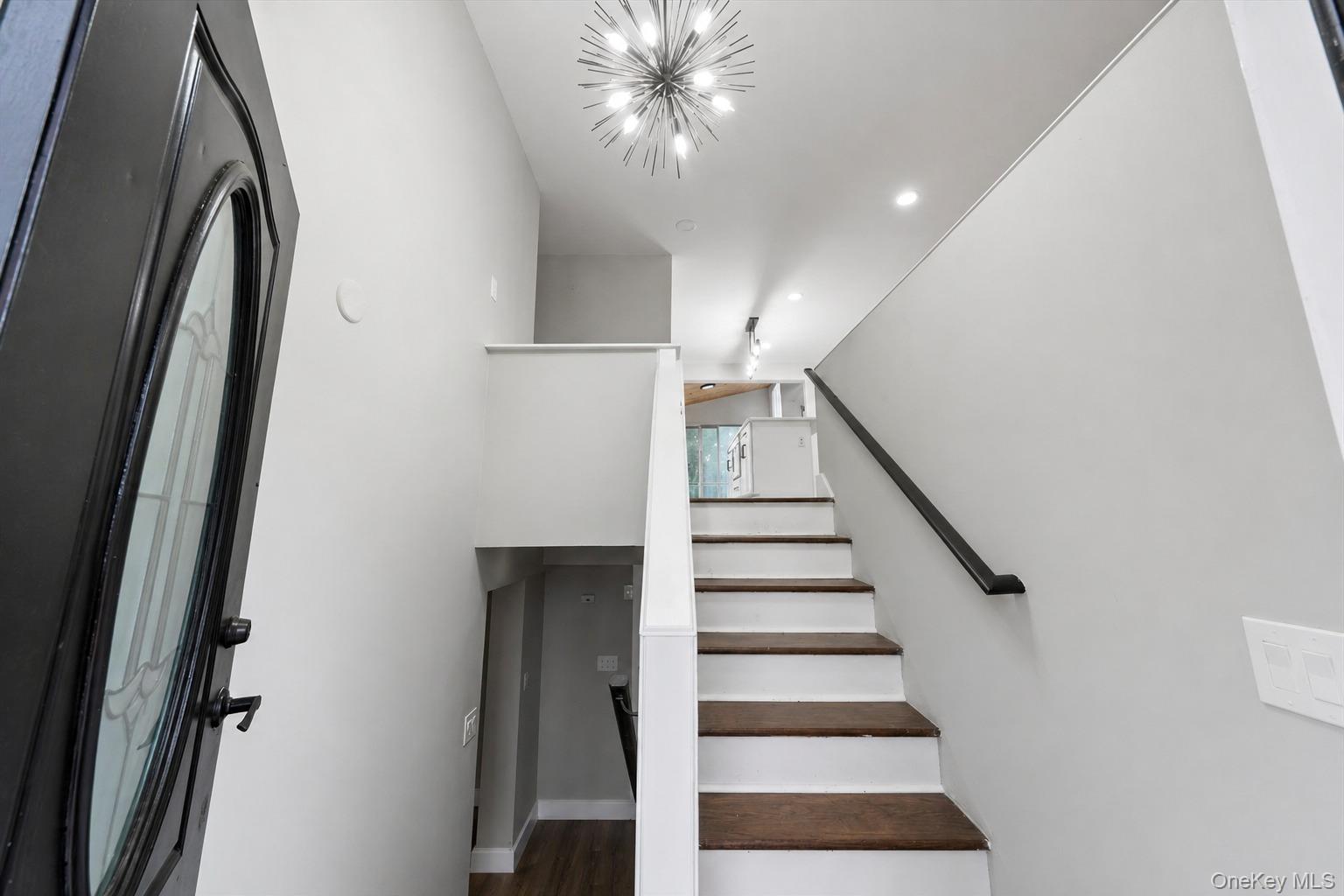 96 Fairmont Road Mahopac, NY 10541 - Photo 3 of 34 Foyer entry with a decorative glass-paneled door, contemporary sputnik chandelier, recessed lighting, and a staircase featuring dark wood-finish treads and a black handrail