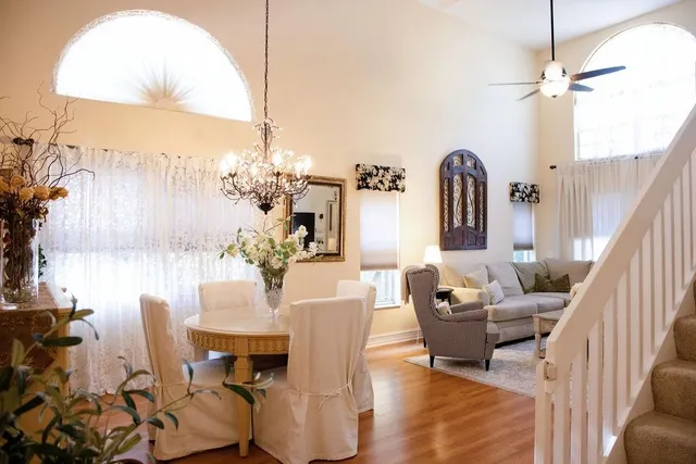 a living room with couches chandelier and a dining table with garden view