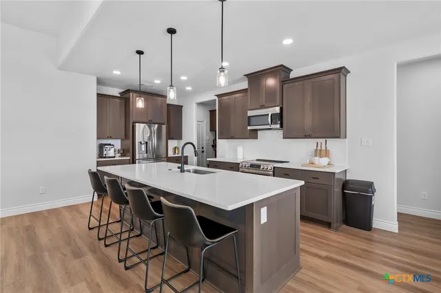 a kitchen with stainless steel appliances granite countertop a sink a stove a refrigerator and island with wooden floor