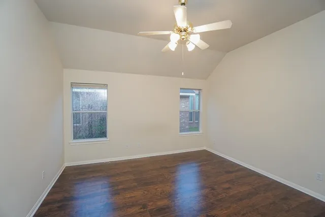 an empty room with wooden floor fan and windows