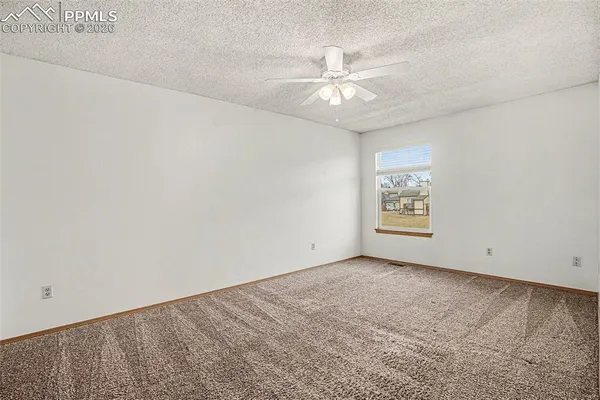 an empty room with a chandelier fan and windows