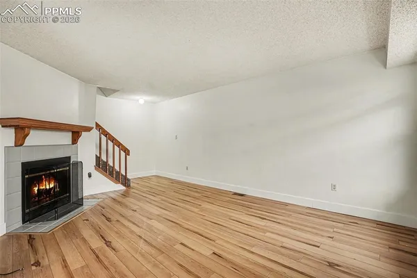 a view of an empty room with wooden floor fireplace and a window
