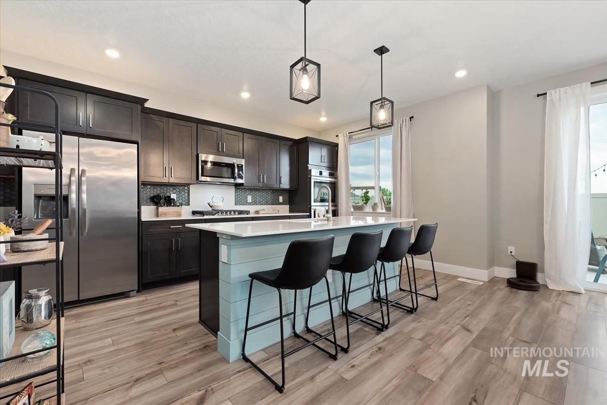 815 Knowledge Street Middleton, ID 83644 - Photo 10 of 49 Open-concept kitchen featuring an oversized island with seating, stainless steel appliances, dark wood cabinetry, a decorative backsplash, and wood-finish flooring