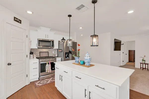a kitchen with stainless steel appliances kitchen island granite countertop a sink a microwave a stove and white cabinets