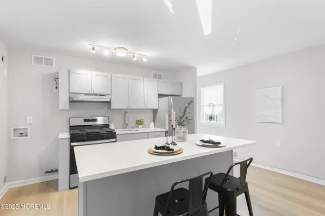 a kitchen with stainless steel appliances a sink a stove a refrigerator white cabinets and wooden floor