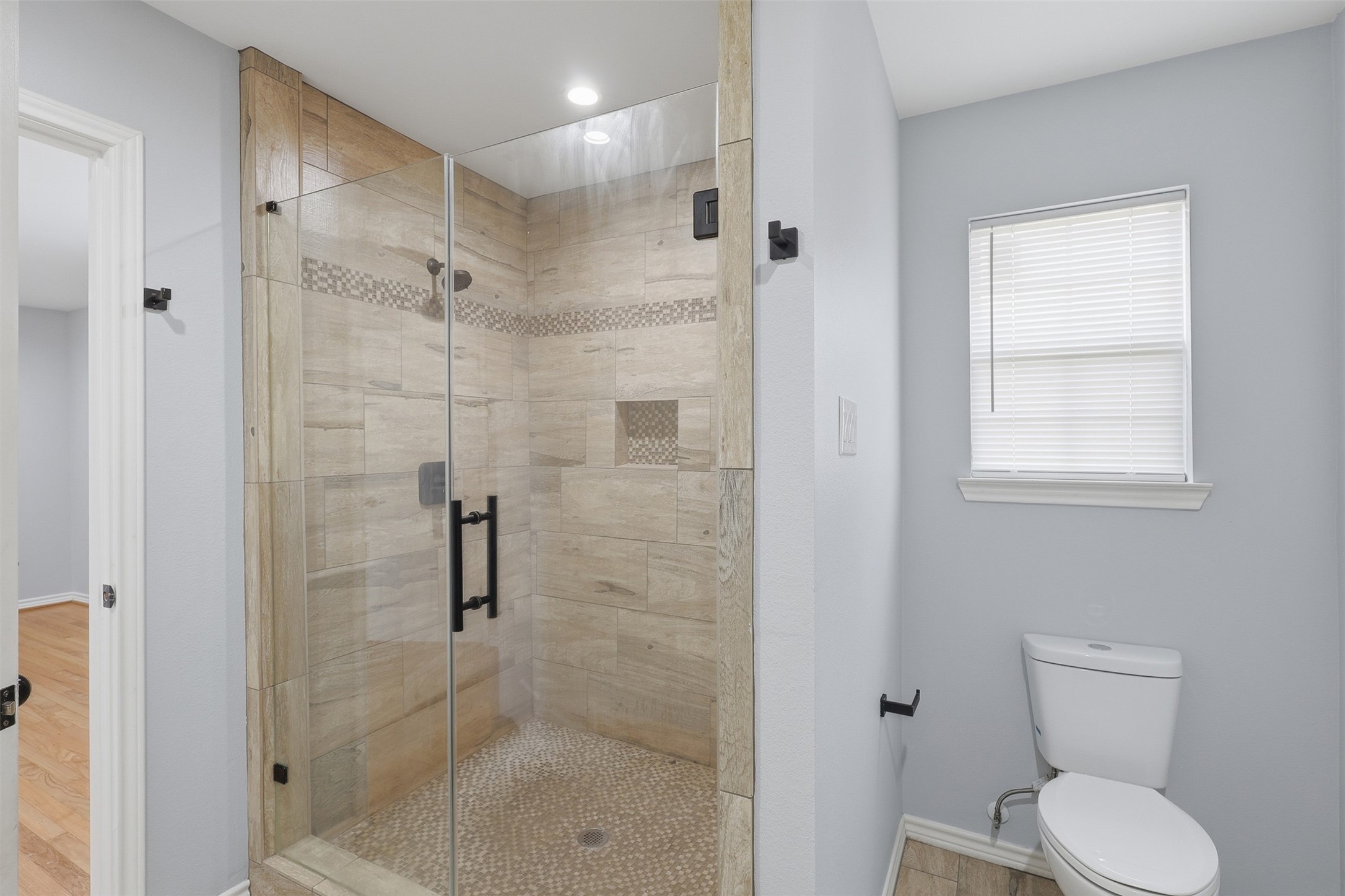 4926 Edfield Street Houston, TX 77033 - Photo 16 of 30 Modern bathroom featuring a stylish glass-enclosed shower with elegant tilework, complemented by a sleek toilet and soft natural light from the window.