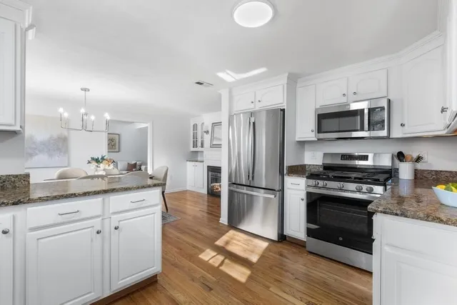 a kitchen with stainless steel appliances granite countertop a refrigerator a stove a sink and white cabinets