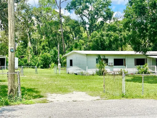 a view of a porch in front of a yard with plants and large trees