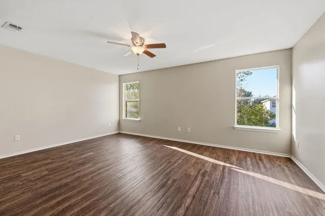 an empty room with wooden floor chandelier fan and windows