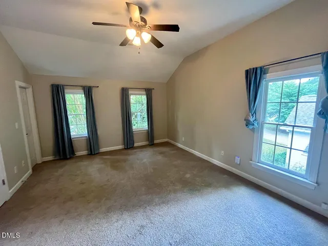 an empty room with chandelier fan and windows