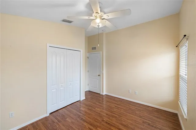 an empty room with wooden floor fan and windows