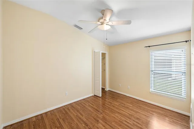 an empty room with wooden floor fan and windows