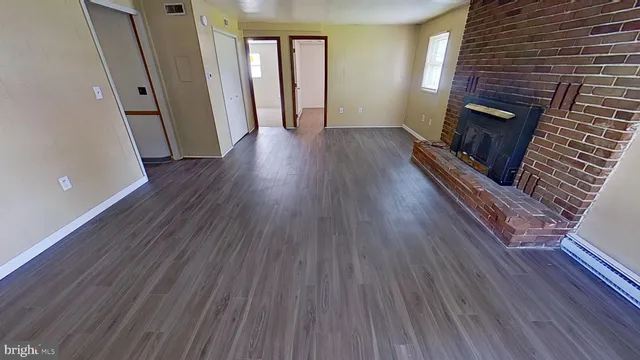 a view of an empty room with wooden floor and a fireplace