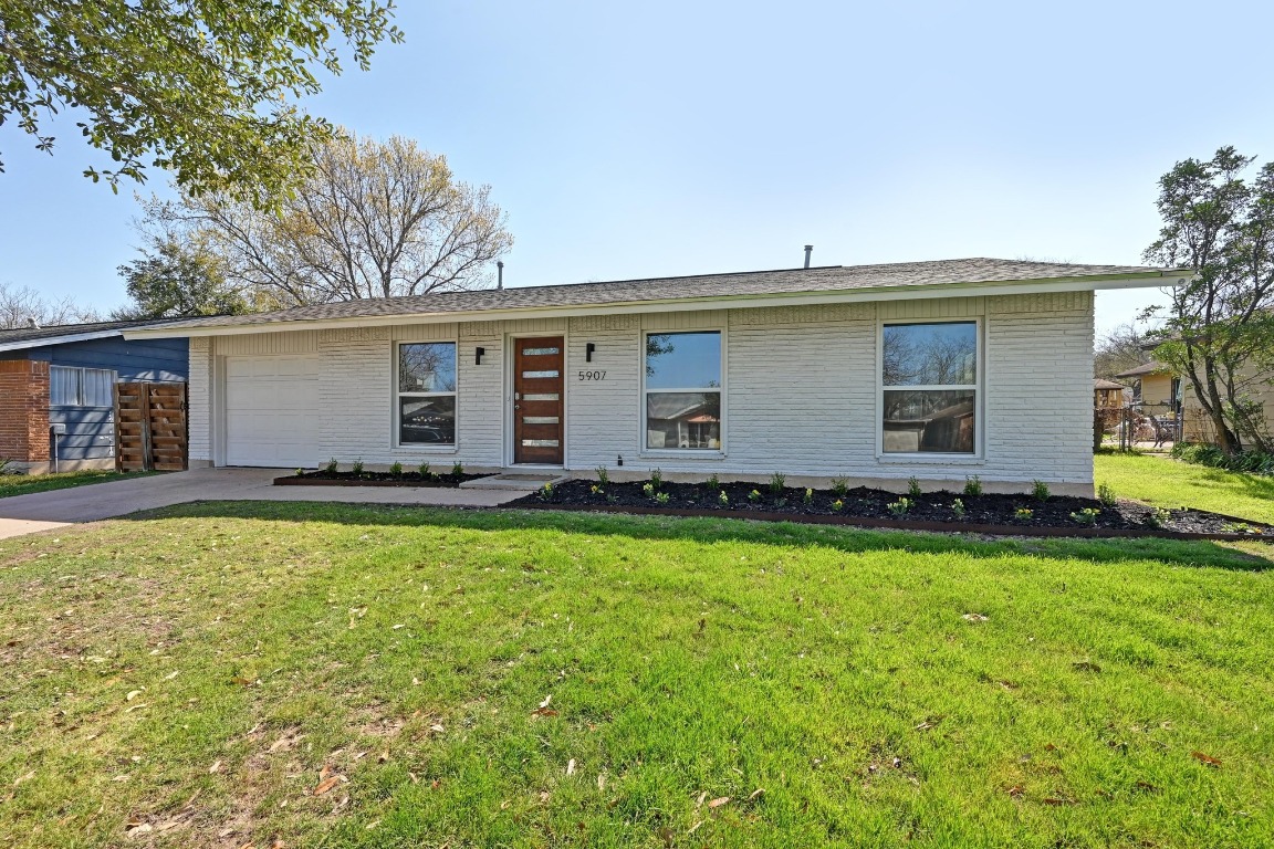 View of front of house with brick siding, an attached garage, concrete driveway, and a front lawn