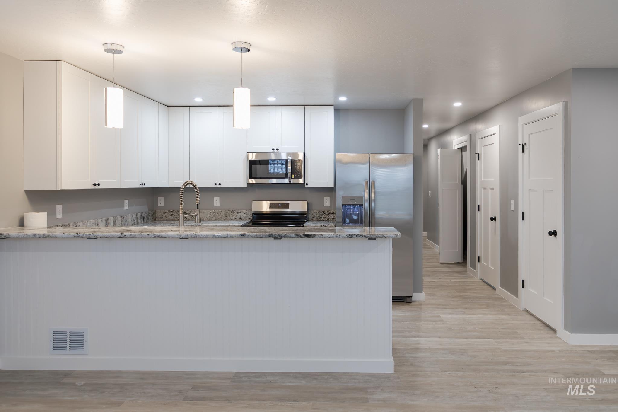 287 Southwest 6th Street, Unit 1 Ontario, OR 97914 - Photo 3 of 49 Kitchen featuring white cabinetry, a peninsula, light stone countertops, stainless steel appliances, and light wood-style flooring