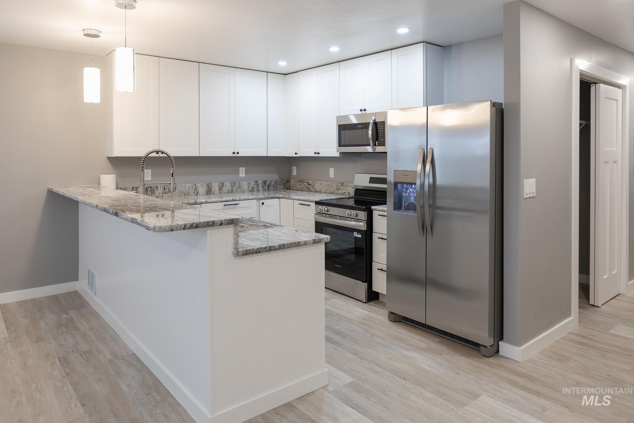 287 Southwest 6th Street, Unit 1 Ontario, OR 97914 - Photo 5 of 49 Kitchen with light stone counters, stainless steel appliances, a peninsula, decorative light fixtures, and white cabinetry