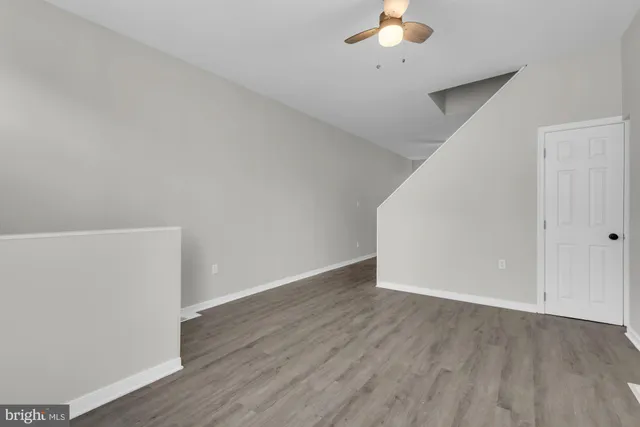an empty room with a chandelier fan and wooden floor