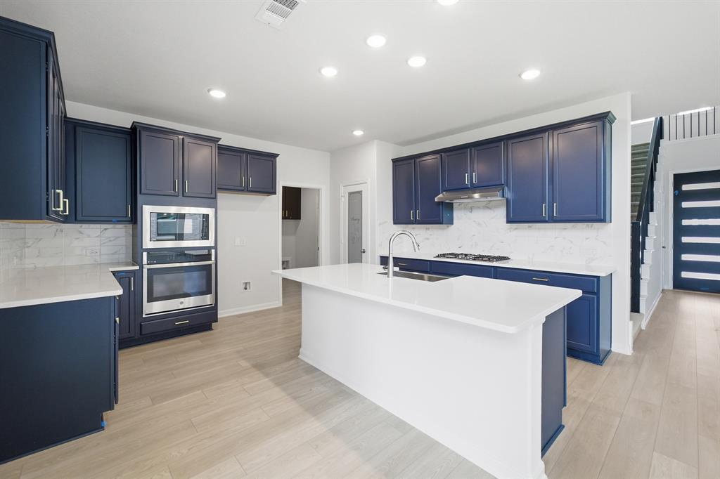 1908 Sangallo Lane Celina, TX 75009 - Photo 24 of 35 Modern kitchen featuring navy cabinetry, a substantial island with a basin sink, light wood-finish flooring, and recessed lighting