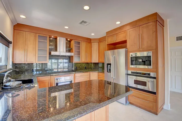 a kitchen with stainless steel appliances granite countertop a refrigerator a stove and a sink with large window