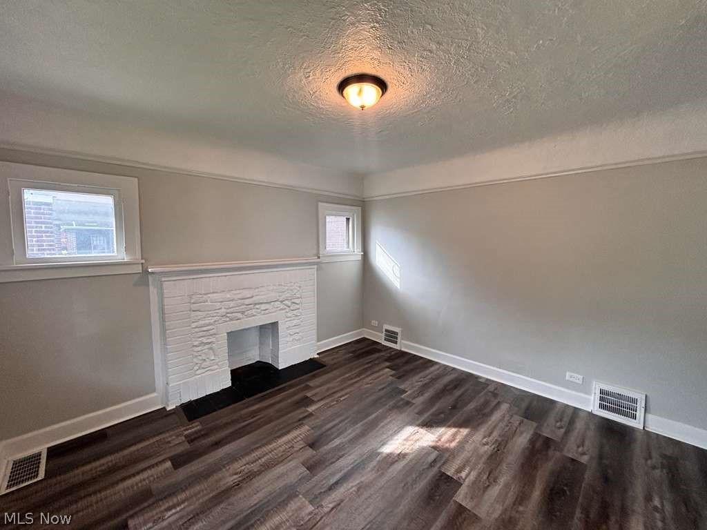 907 Rondel Road Cleveland, OH 44110 - Photo 26 of 26 Room featuring a painted brick fireplace with a dark hearth, wood-finish flooring, and two windows providing natural light