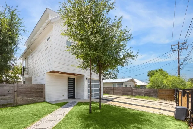 a view of a small house in front of a house with wooden fence and large tree