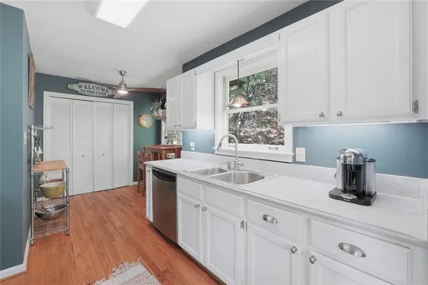 a kitchen with a sink dishwasher and white cabinets with wooden floor
