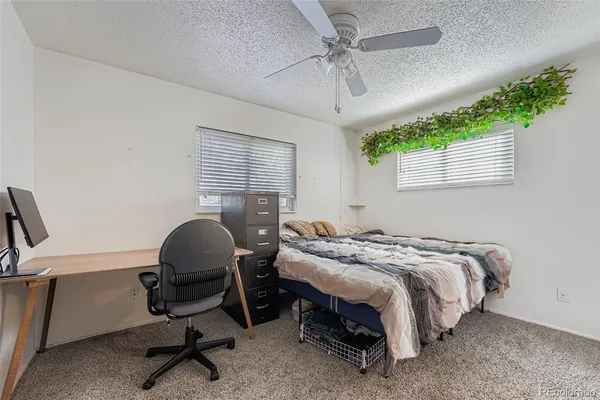a bedroom with a bed a desk chair and windows