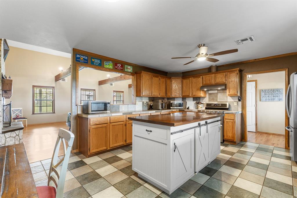 13315 Highway 281 Scotland, TX 76379 - Photo 9 of 40 Spacious kitchen featuring an island with a wood-finish countertop, light wood cabinetry, a tile backsplash, and checkerboard tile flooring