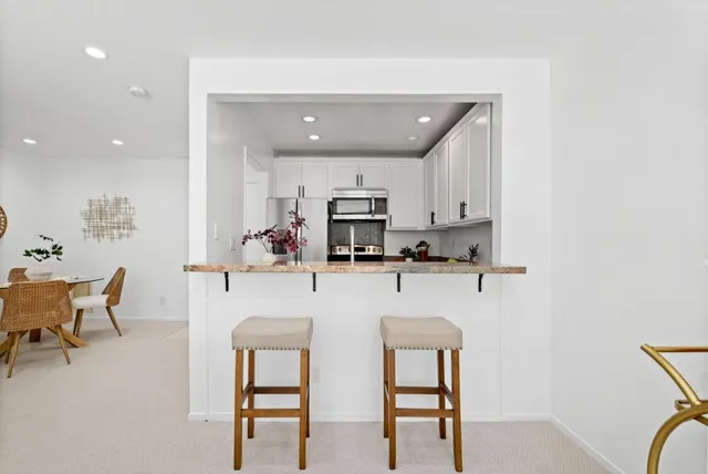 a kitchen with stainless steel appliances granite countertop a dining table chairs refrigerator and sink