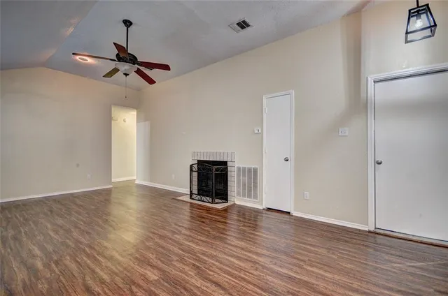 an empty room with wooden floor fireplace and windows