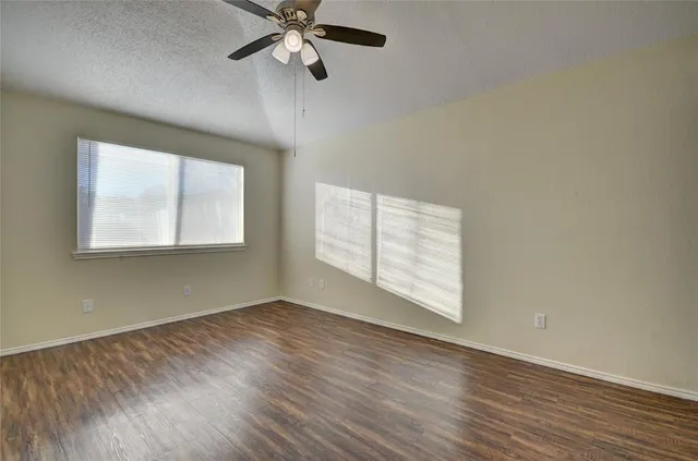 an empty room with wooden floor chandelier fan and windows