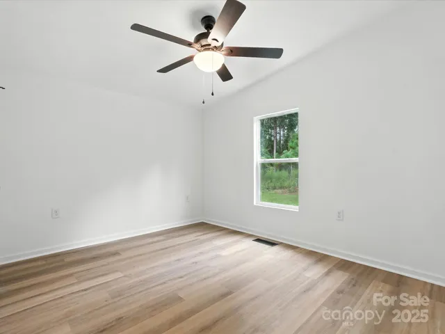 an empty room with wooden floor fan and windows
